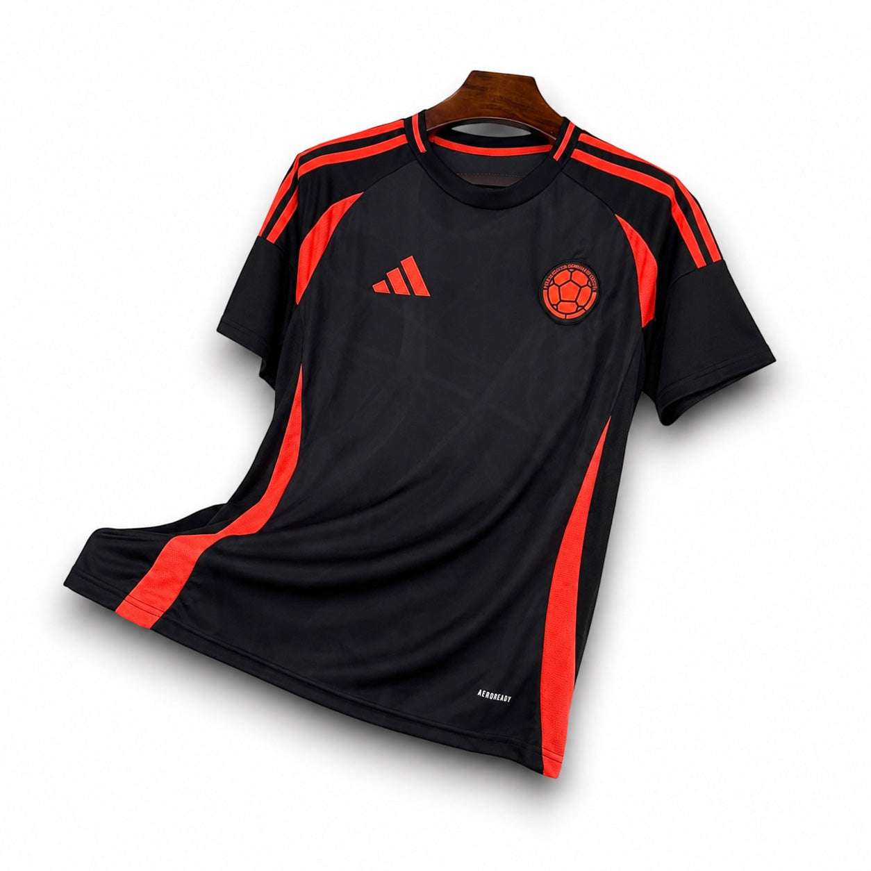 Leazofoot Colombia 2024 away soccer jersey in black with bright orange accents and team crest on a wooden hanger.