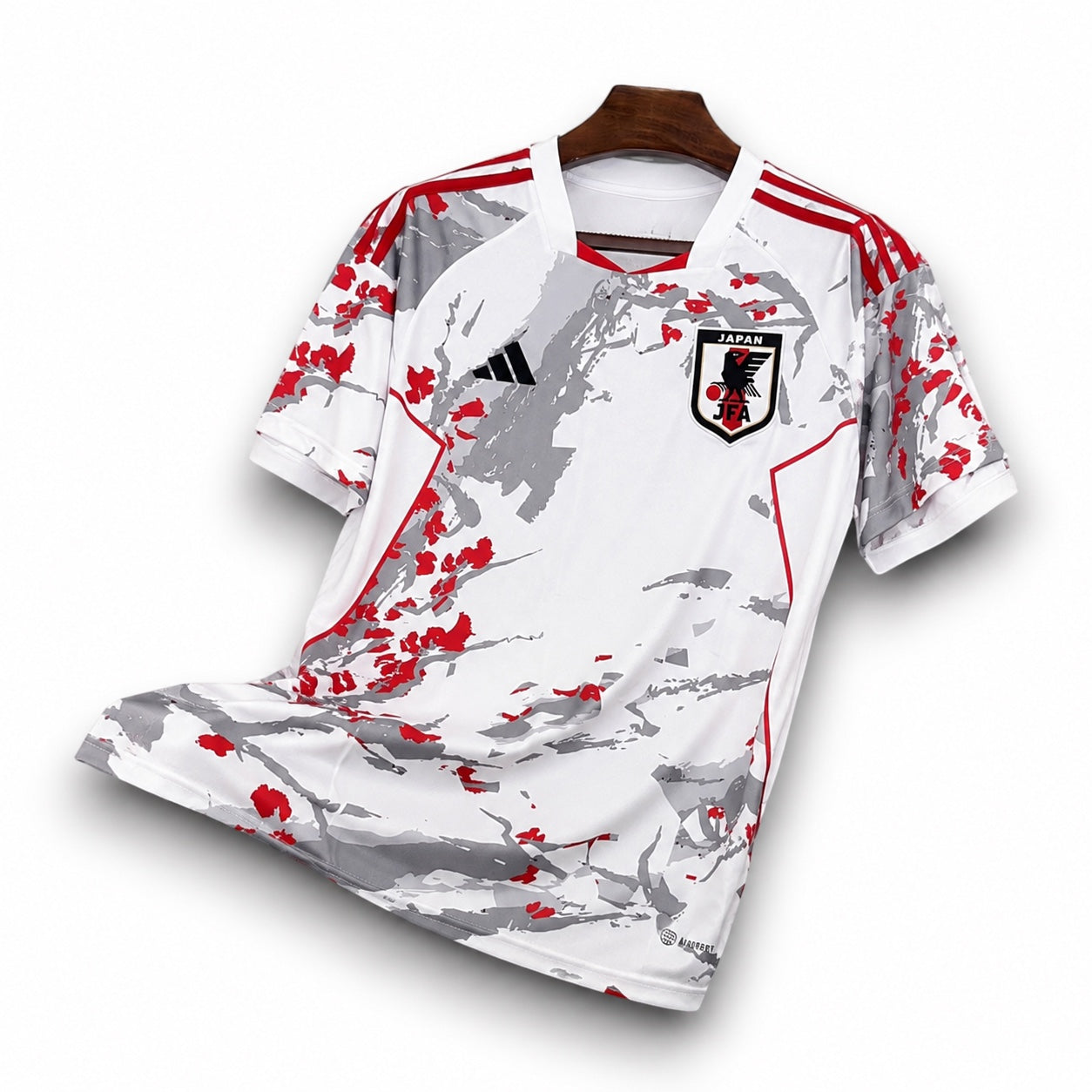Leazofoot Japan 2024 concept football jersey in white with grey and red abstract graphic pattern on a wooden hanger