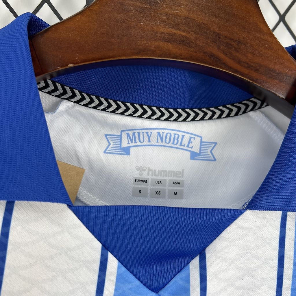 Leazofoot Malaga 26/27 home football jersey featuring blue and white stripes with Muy Noble inner neck detail.