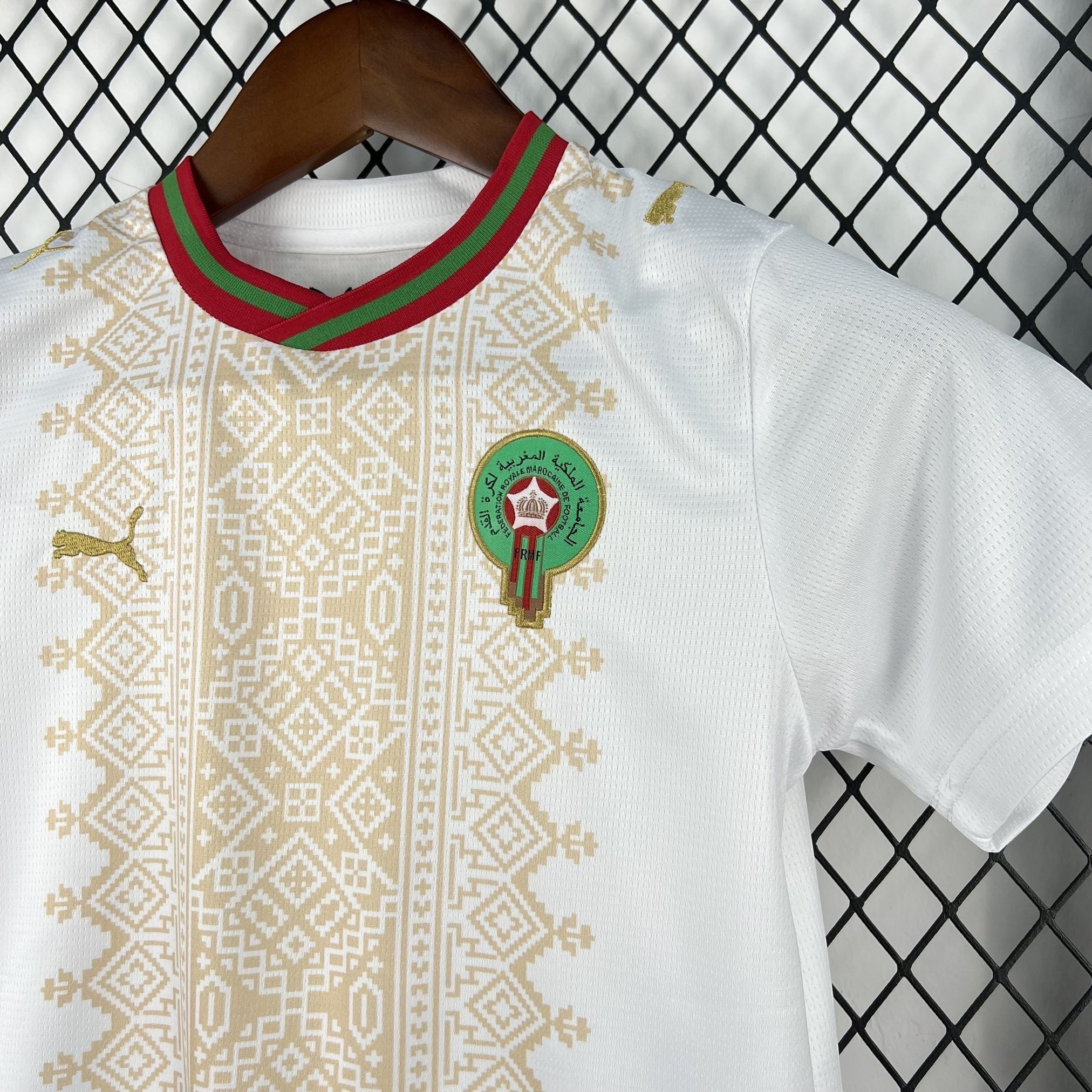 Leazofoot white children's football jersey with gold Puma logo and Moroccan crest, featuring a red and green striped collar and intricate gold geometric pattern.