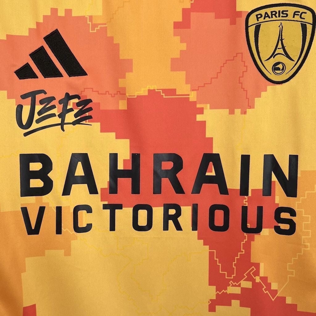 Leazofoot Paris FC 25/26 third jersey in yellow and orange with pixelated pattern, black logos, and sponsor text.