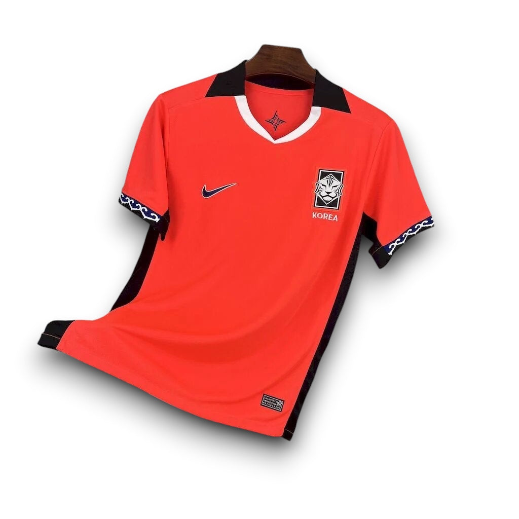 Leazofoot South Korea 2026 home soccer jersey in vibrant orange with black collar and white trim. Features team crest and Nike logo.