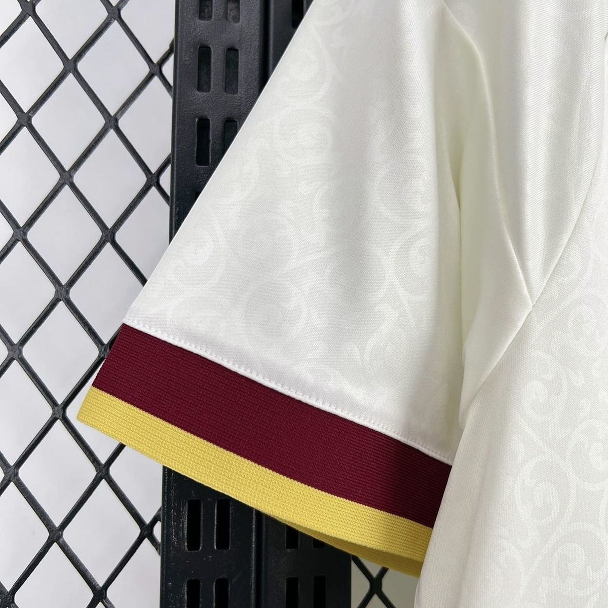 Leazofoot Spain 2026 away jersey sleeve detail featuring white fabric with subtle pattern, maroon and yellow trim.