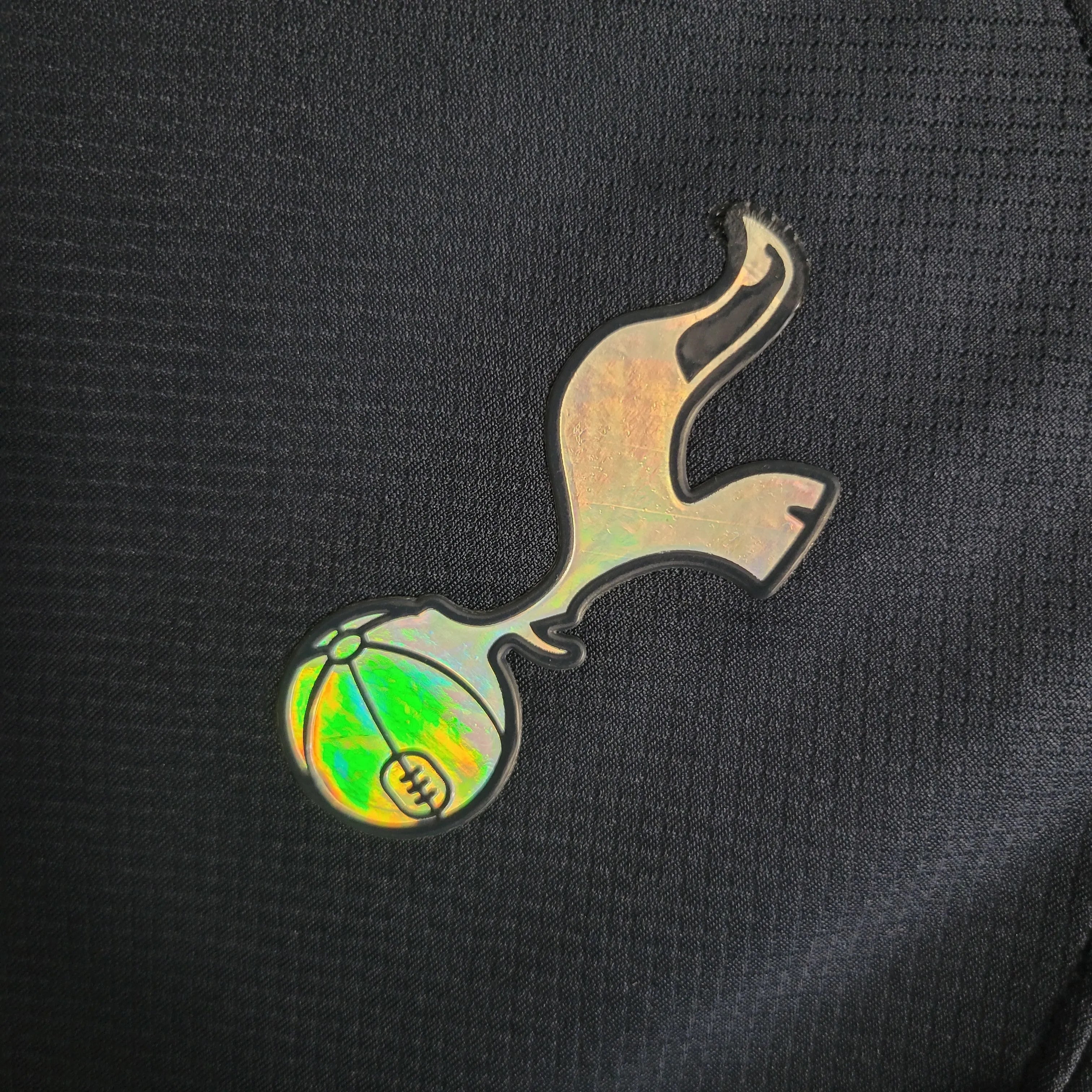 Leazofoot Tottenham 23/24 away jersey crest with iridescent detail on black fabric.