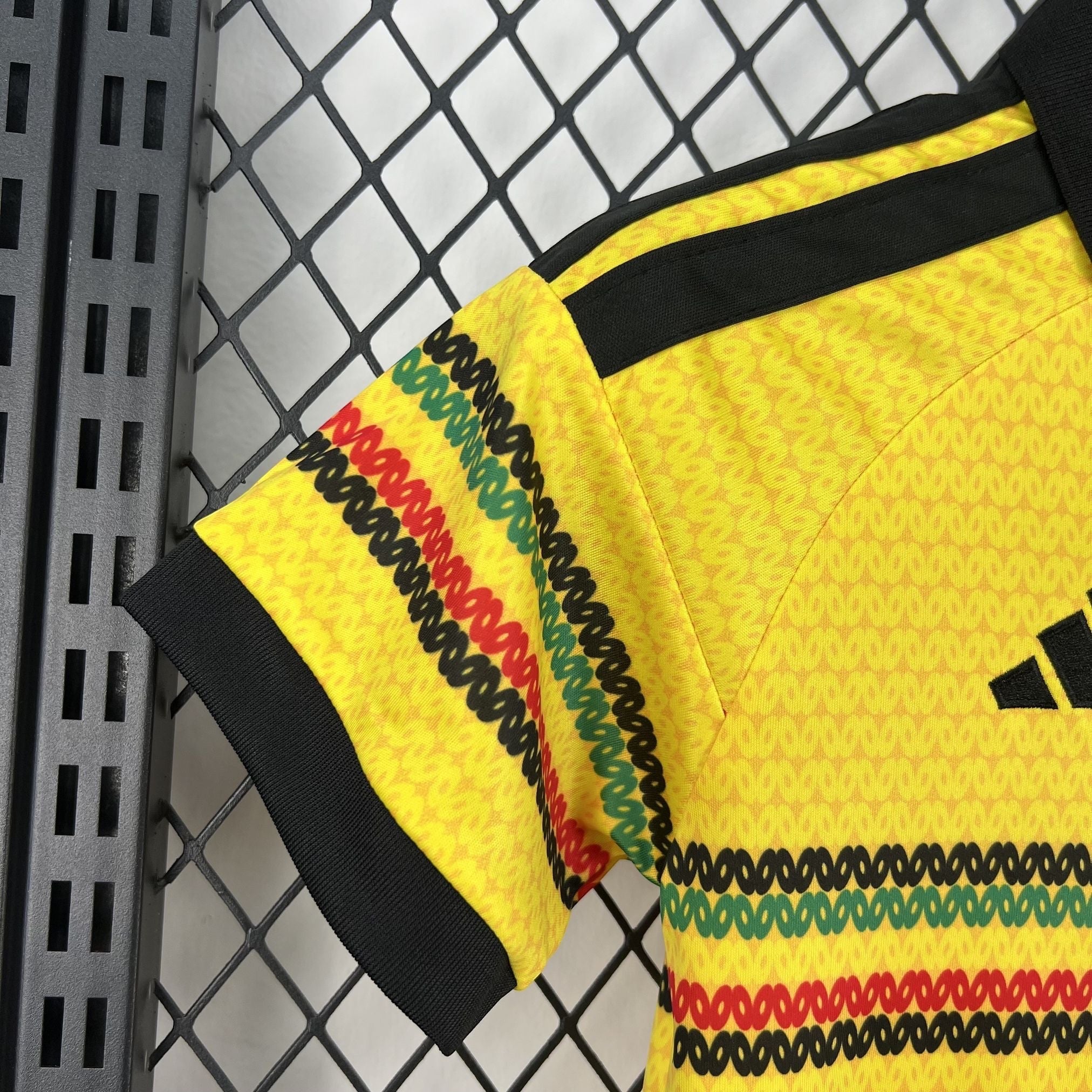 Leazofoot Jamaica 2026 kids home jersey in yellow with black, green, and red patterned sleeve and shoulder details.