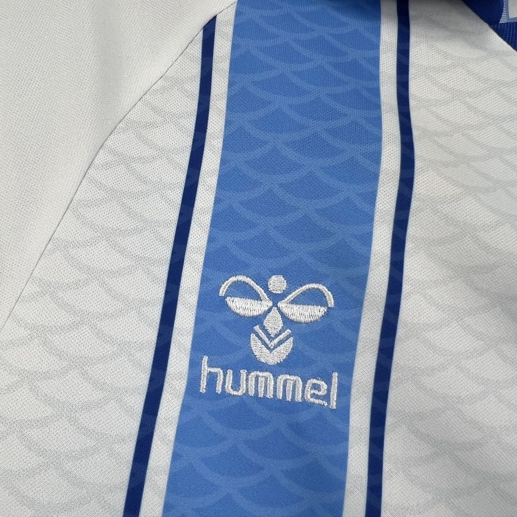 Leazofoot Malaga 26/27 home football jersey featuring white and blue textured fabric with embroidered Hummel logo.