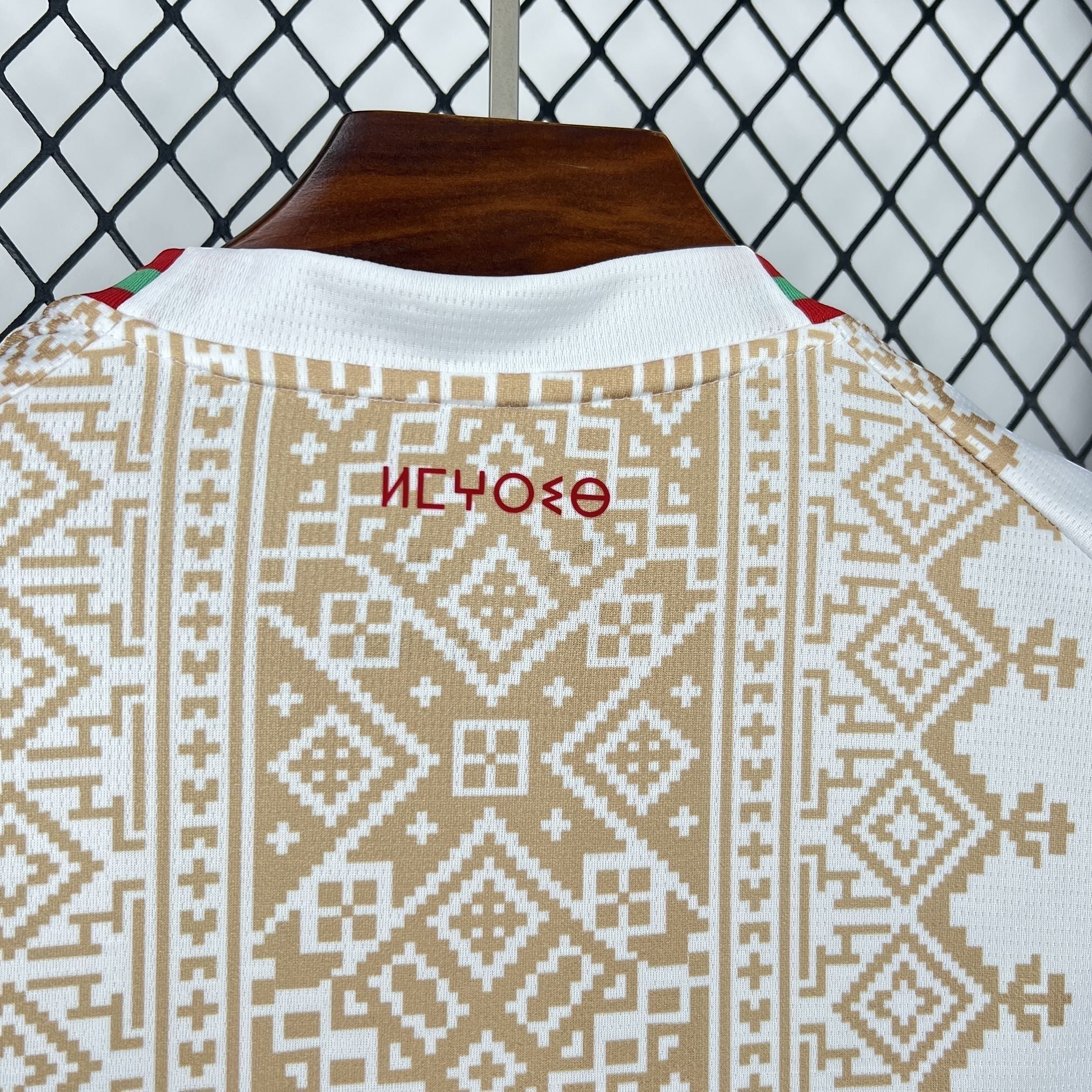 Leazofoot MAROC 2026 away football jersey. White with intricate gold geometric pattern inspired by Moroccan art. Red and green trim on collar.