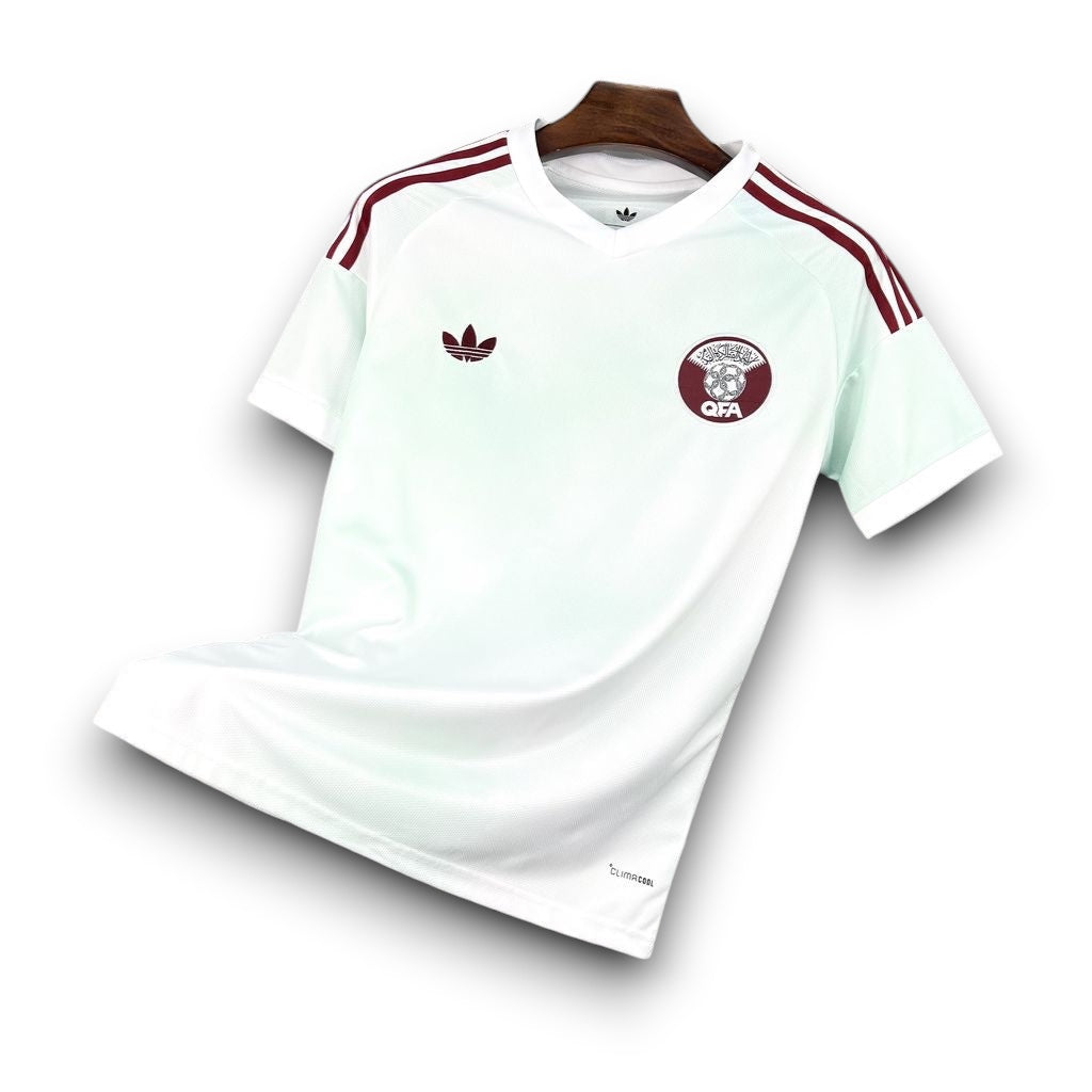 Leazofoot Qatar 2026 away soccer jersey in white with maroon stripes and QFA crest on a black grid display.