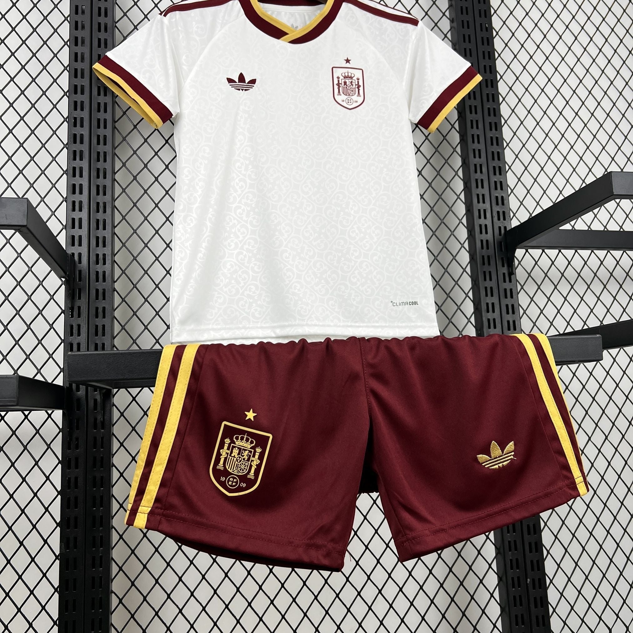 Leazofoot Spain kids' white soccer jersey with maroon and gold trim and maroon shorts with gold stripes.